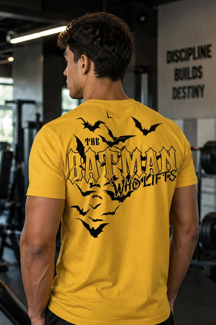 Person wearing a yellow t-shirt with black text and bats in a gym setting